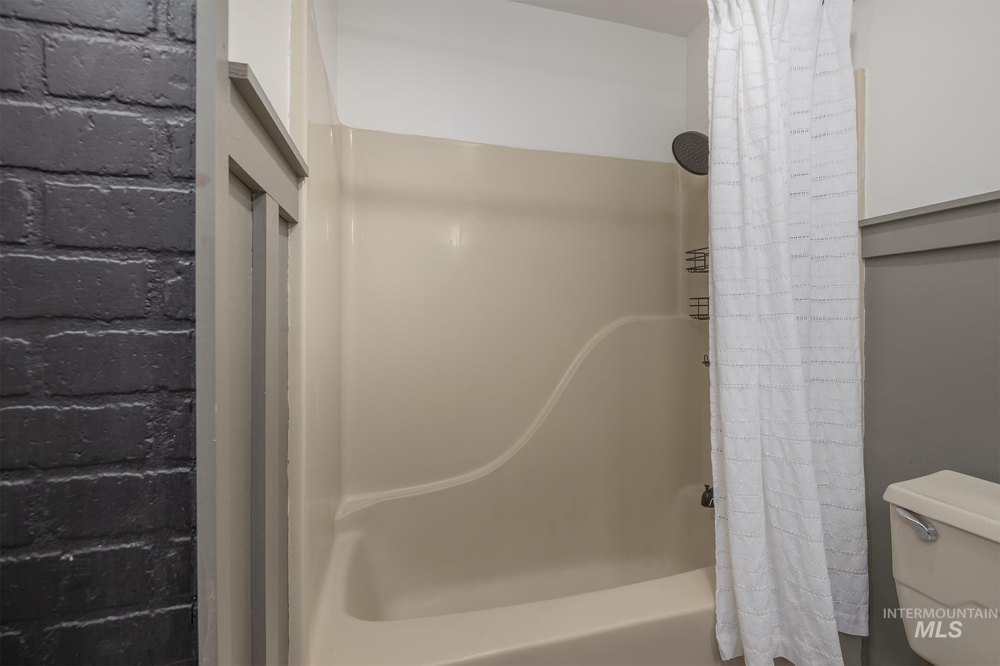 61 Southwest 4th Street Ontario, OR 97914 - Photo 25 of 42 Bathtub and shower combination featuring a beige surround, dark finish shower head, and an adjacent toilet