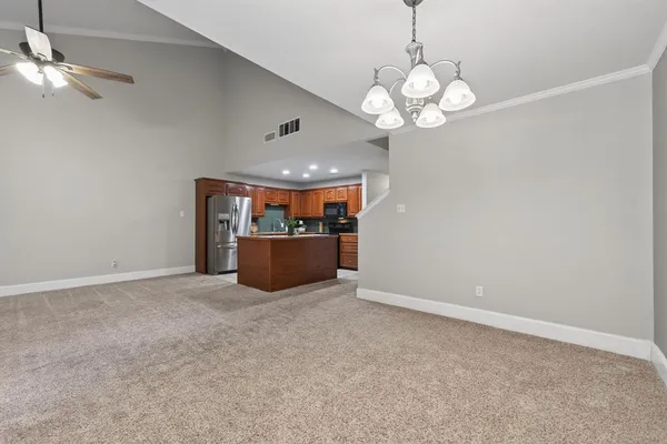 an empty room with a chandelier fan and kitchen view