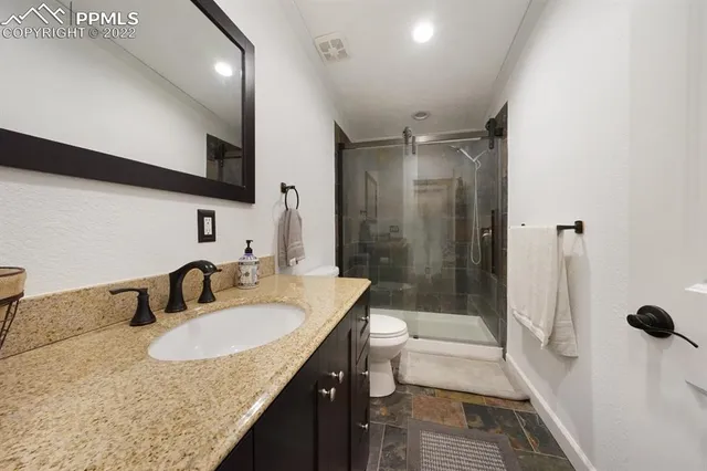 a bathroom with a granite countertop sink a toilet a mirror and shower