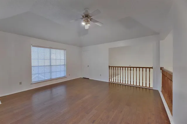 a view of an empty room with wooden floor and fan