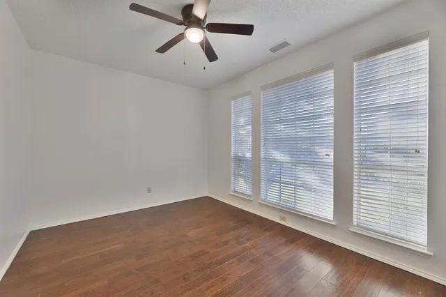 an empty room with wooden floor chandelier fan and windows