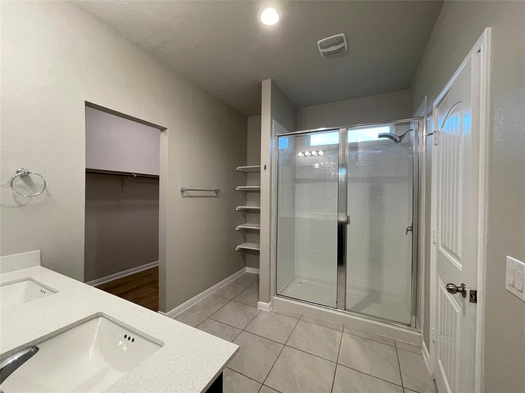 6717 Ranchito Drive Austin, TX 78744 - Photo 14 of 28 Bathroom featuring double vanity, a spacious closet, a shower stall, and light tile patterned floors
