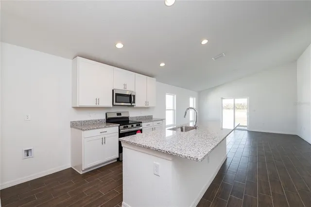a kitchen with granite countertop a sink a stove top oven a counter space and cabinets