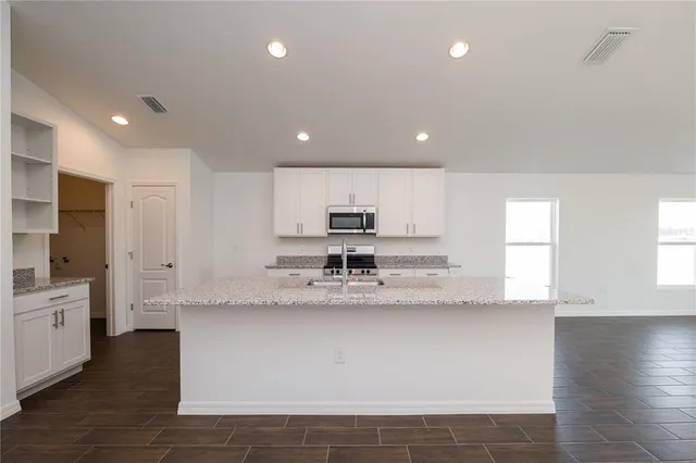 a large kitchen with stainless steel appliances a large counter top a stove and a refrigerator