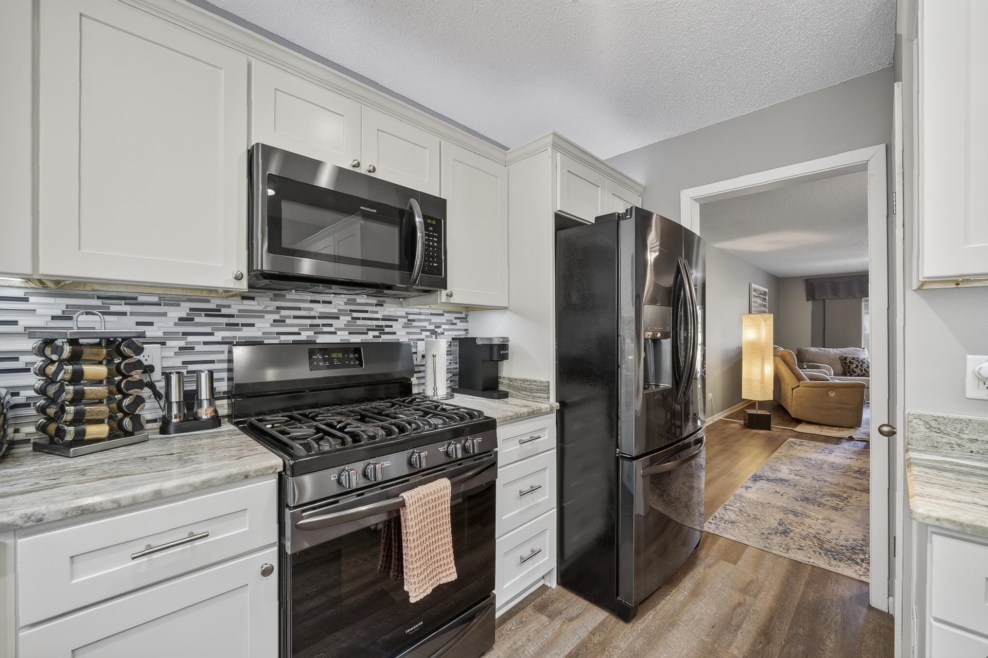 74 Driftwood Road Counce, TN 38326 - Photo 10 of 40 Kitchen featuring white cabinetry, granite countertops, a tiled backsplash, and stainless steel appliances including an oven with gas cooktop, microwave, and refrigerator