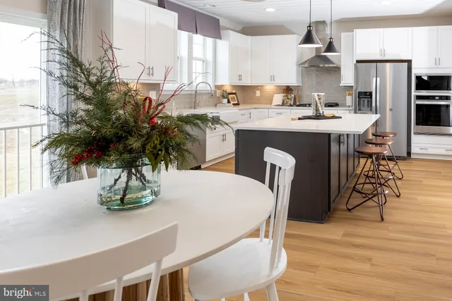 a kitchen with stainless steel appliances kitchen island granite countertop a stove a refrigerator a sink a dining table and chairs with wooden floor