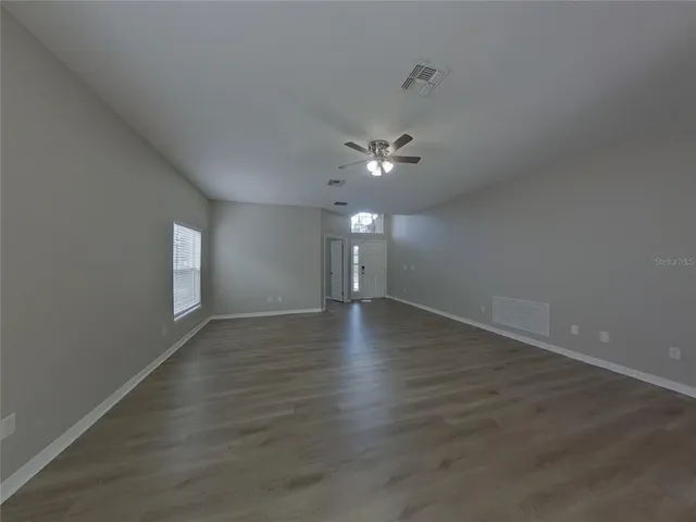 a view of an empty room with wooden floor and fan