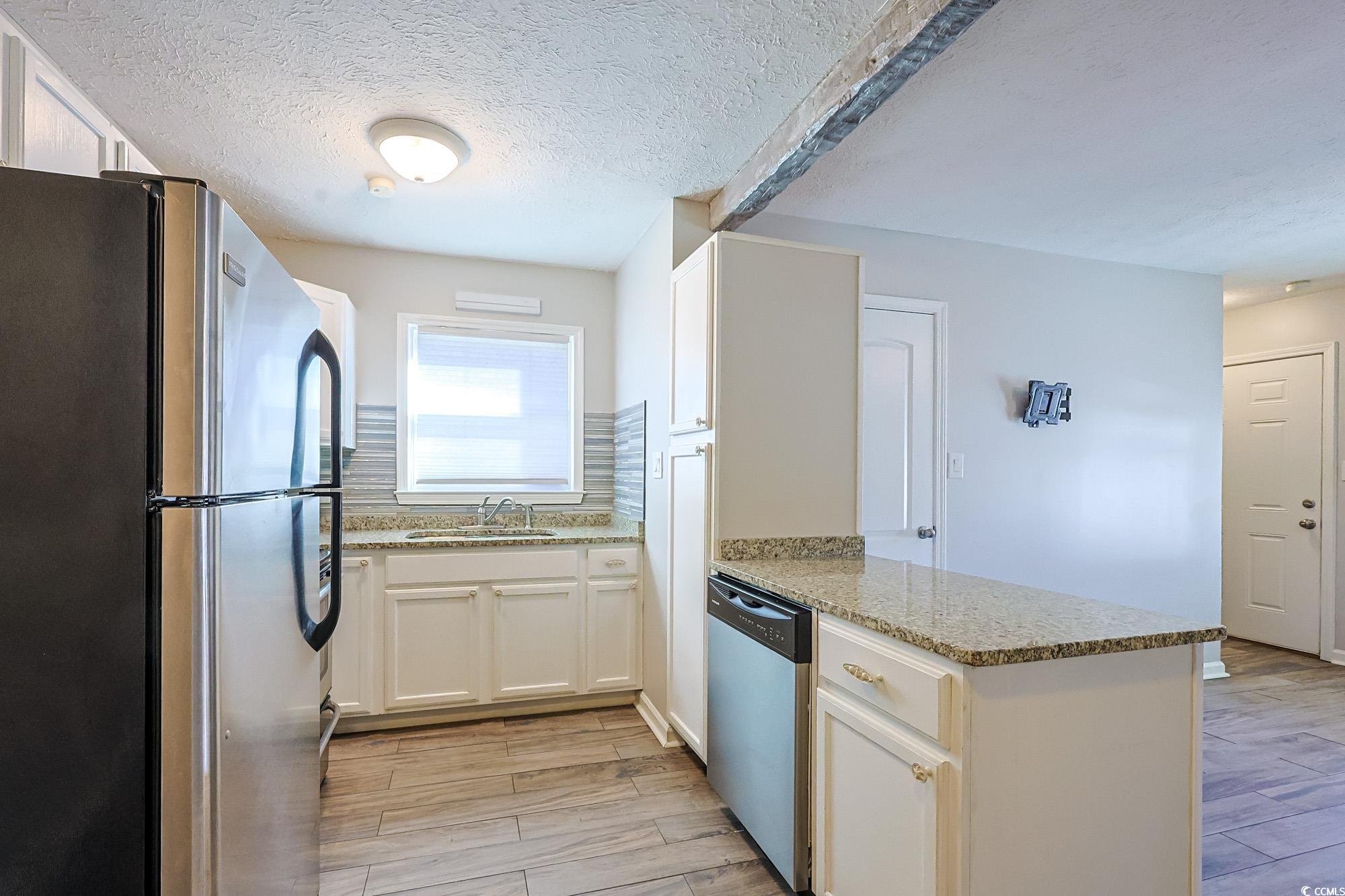 718 Juniper Drive Surfside Beach, SC 29575 - Photo 6 of 18 Kitchen featuring appliances with stainless steel finishes, white cabinetry, a textured ceiling, wood finish floors, and light stone counters