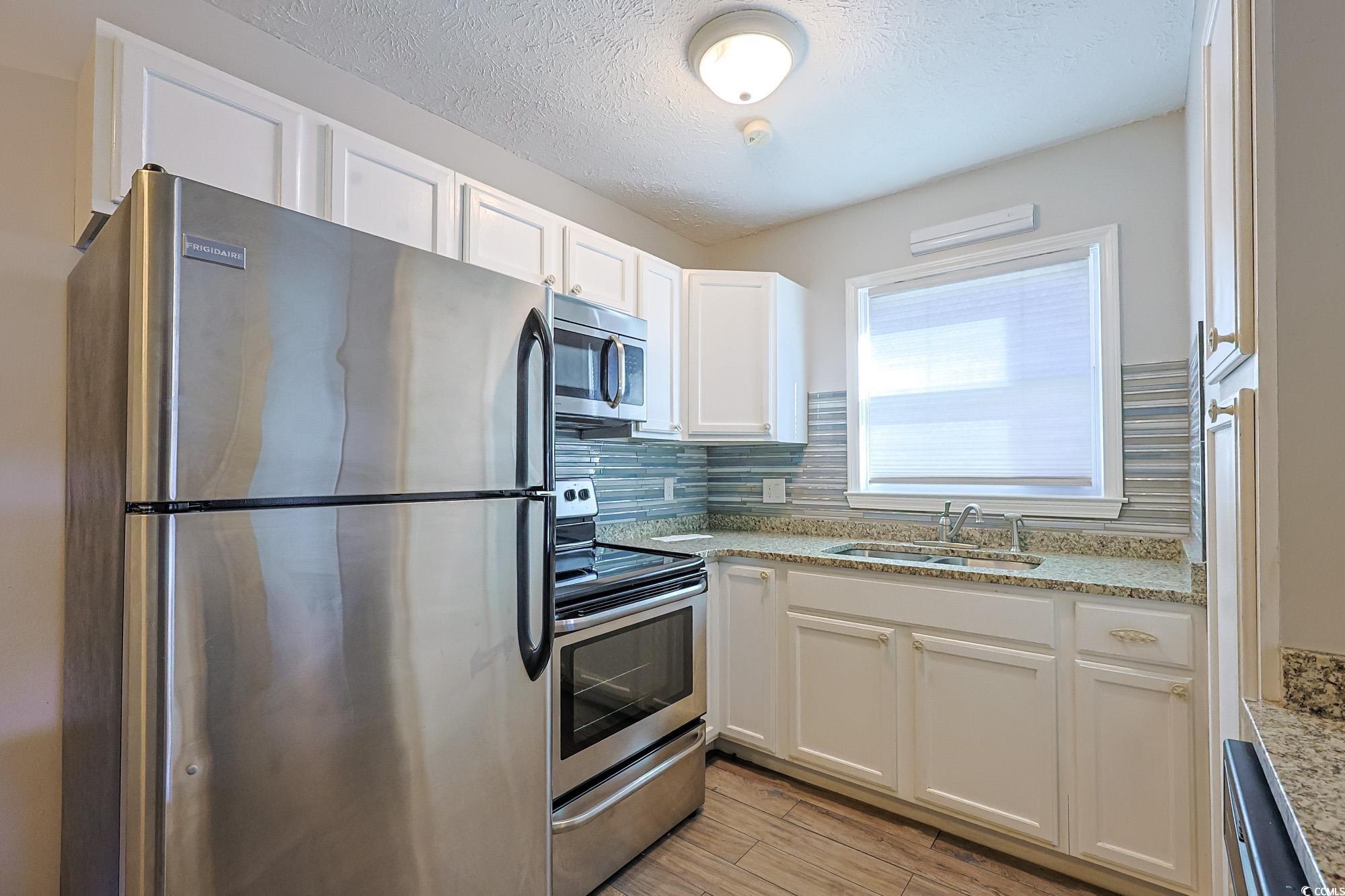 718 Juniper Drive Surfside Beach, SC 29575 - Photo 7 of 18 Kitchen with appliances with stainless steel finishes, a textured ceiling, white cabinets, backsplash, and light wood-type flooring