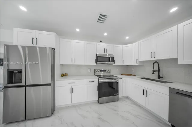a kitchen with stainless steel appliances granite countertop a refrigerator sink and white cabinets
