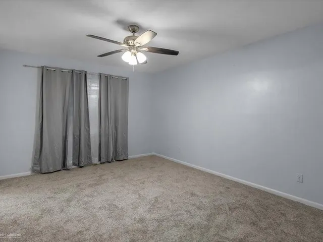 an empty room with a chandelier fan and windows