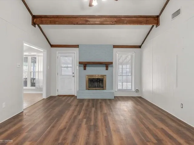 a view of an empty room with wooden floor fireplace and a window