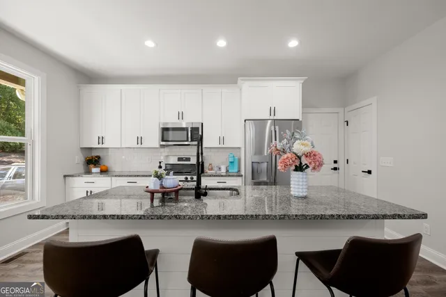 a kitchen with stainless steel appliances granite countertop a table chairs sink and cabinets