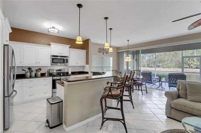 a open kitchen with stainless steel appliances granite countertop a stove top oven a sink a dining table and chairs with white cabinets