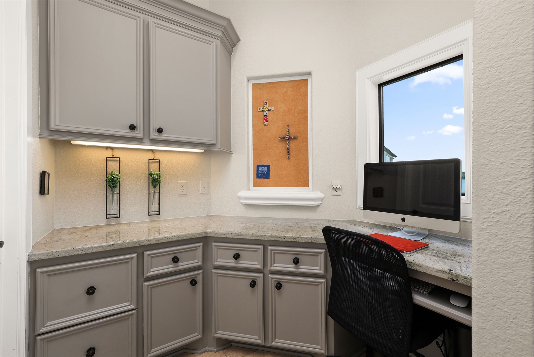 10896 Decatur Street Willis, TX 77318 - Photo 29 of 50 Discover a cozy home office nook featuring elegant gray cabinetry, granite countertops, and a sunlit window—complete with a corkboard and ample space for a computer setup, perfect for a serene work environment.