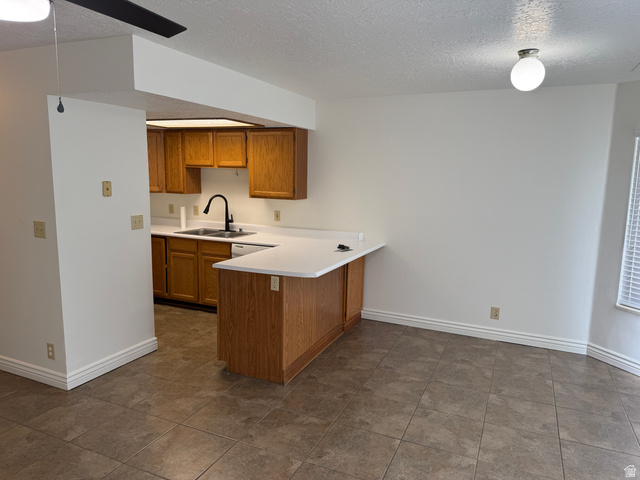 747 Hanover Drive Orem, UT 84058 - Photo 5 of 30 Kitchen featuring a textured ceiling, wood finish cabinetry, light countertops, a peninsula, and dark tile patterned flooring