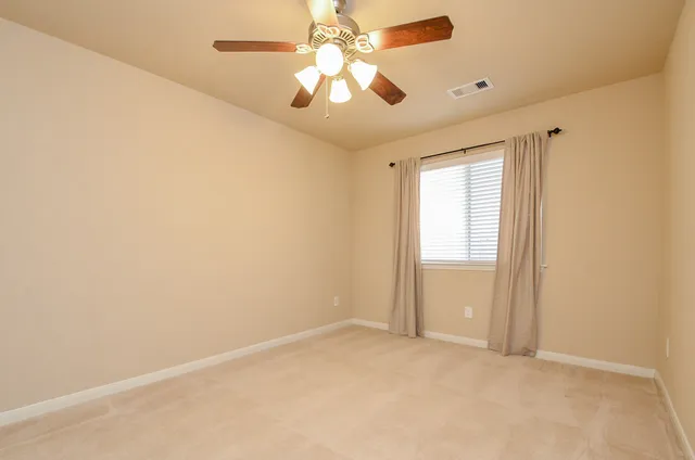 an empty room with a chandelier fan and windows