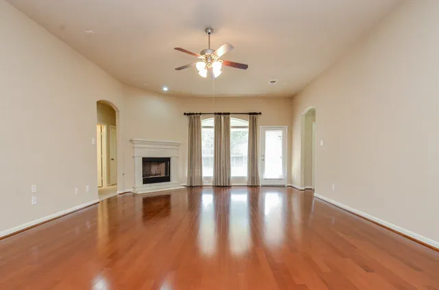 a view of an empty room with wooden floor fireplace and a window