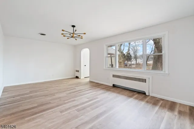 an empty room with wooden floor chandelier fan and windows