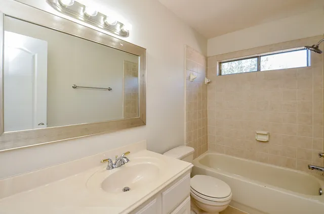 a bathroom with a bathtub shower sink vanity mirror and toilet