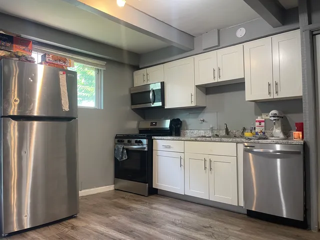 a kitchen with stainless steel appliances granite countertop a refrigerator a sink dishwasher a stove and white cabinets with wooden floor