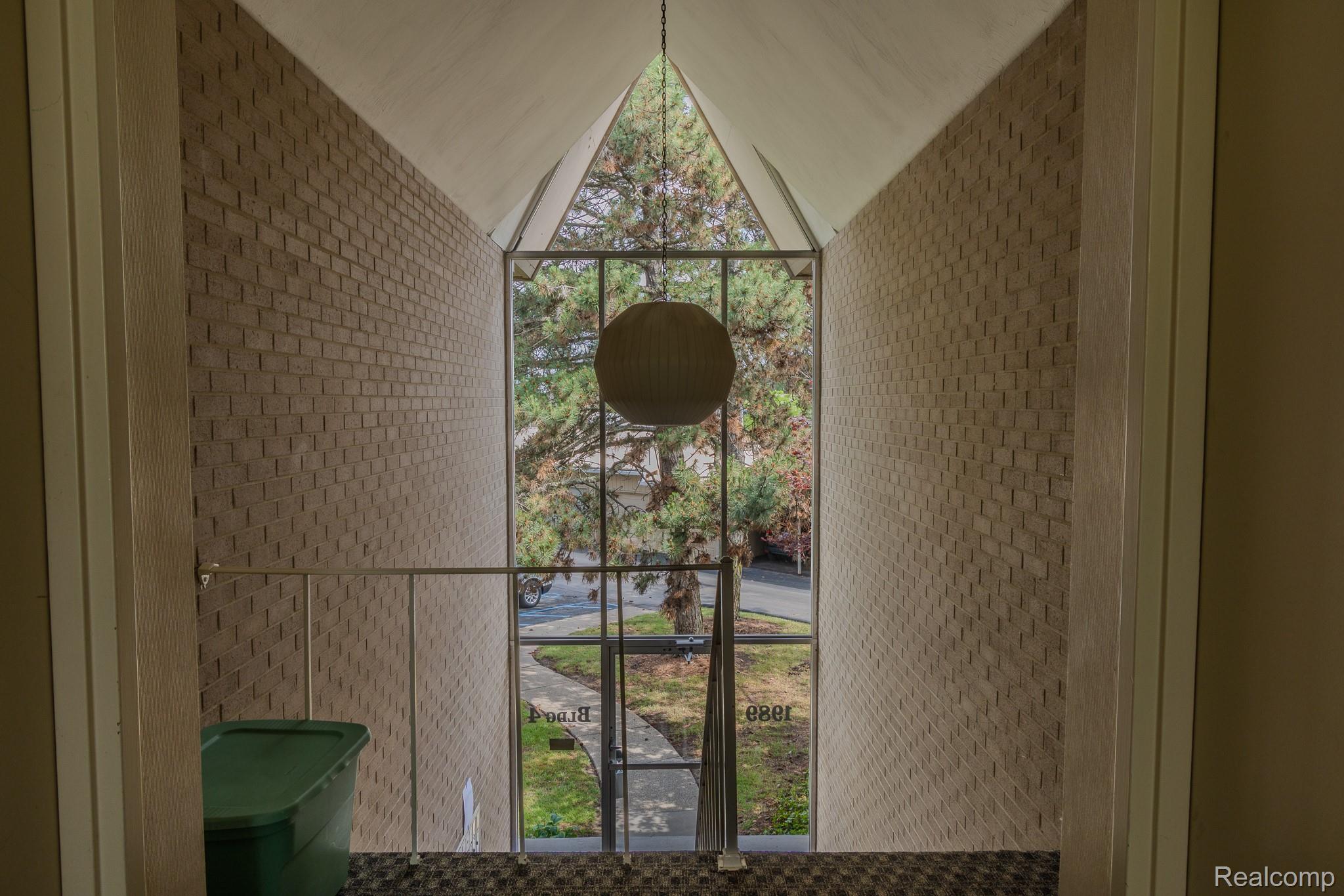 1989 Klingensmith Road, Unit 46 Bloomfield Hills, MI 48302 - Photo 33 of 41 Two-story entry foyer featuring a full-height window wall with grid pattern, a spherical pendant light, and light-toned brick accent walls