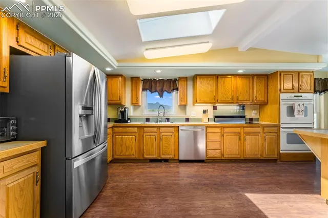 a kitchen with stainless steel appliances granite countertop a refrigerator a sink dishwasher a stove and white countertops with wooden floor