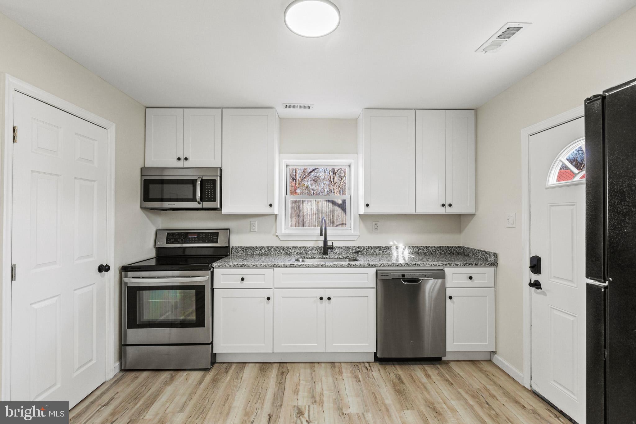 7764 Port Tobacco Road Port Tobacco, MD 20677 - Photo 4 of 14 a kitchen with stainless steel appliances granite countertop a stove top oven a sink dishwasher and a refrigerator with wooden floor