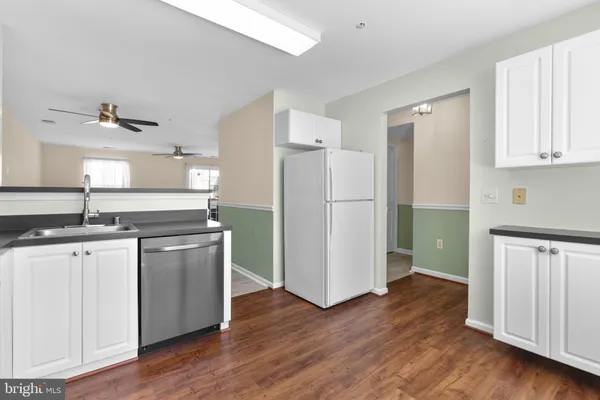 a kitchen with stainless steel appliances granite countertop a refrigerator a sink and white cabinets with wooden floor