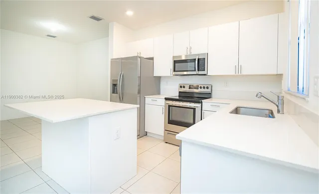 a kitchen with stainless steel appliances a microwave a stove a sink a refrigerator and white cabinets