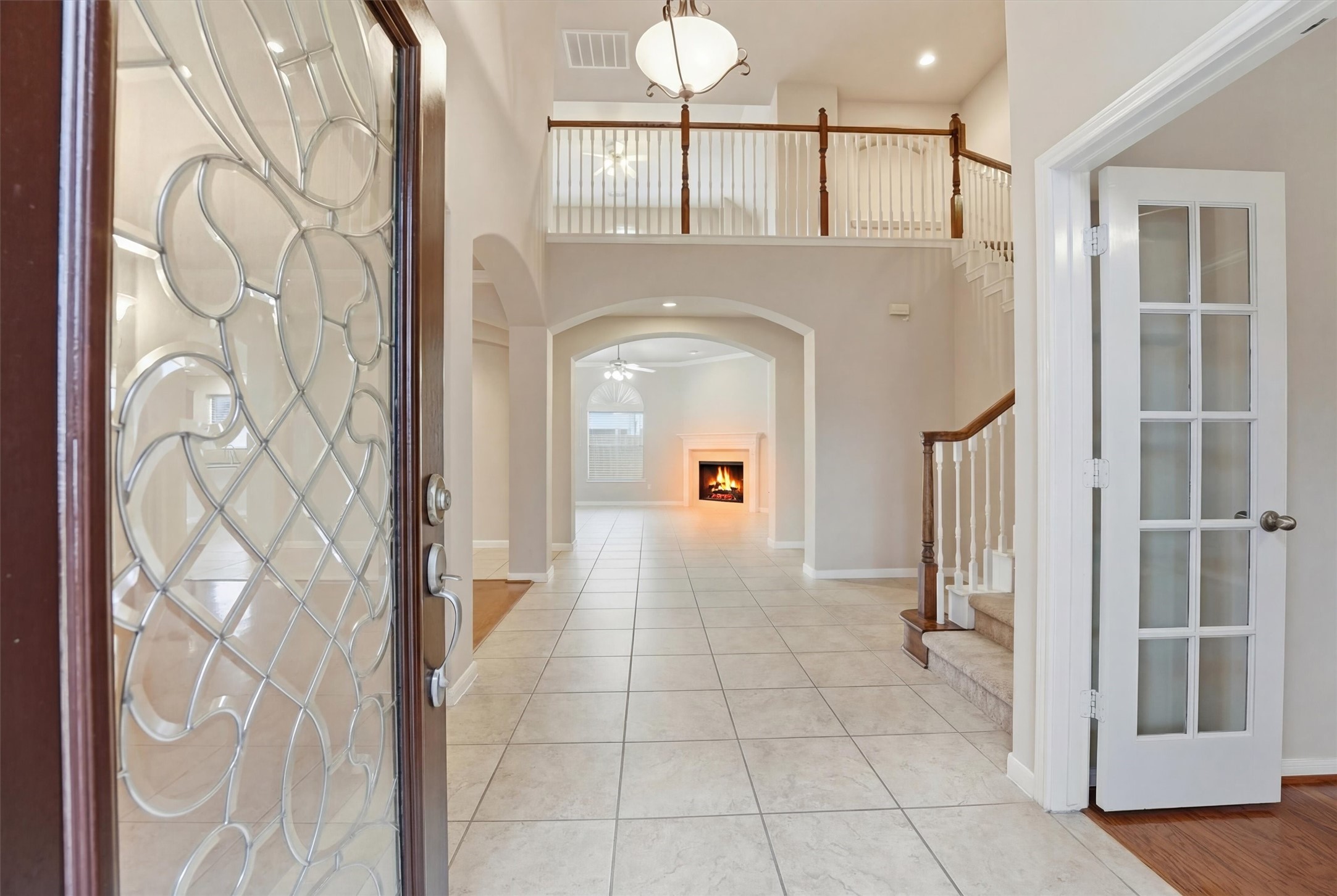 17415 Memorial Mills Drive Spring, TX 77379 - Photo 3 of 39 A bright, welcoming entry opens to soaring ceilings, arched openings, and an elegant second-floor overlook. Tile flooring extends through the main living areas, complemented by a sweeping staircase with wood accents and a gas fireplace anchoring the living space beyond.
