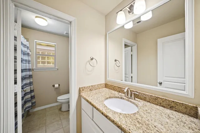 a bathroom with a granite countertop double vanity sink a mirror and a toilet