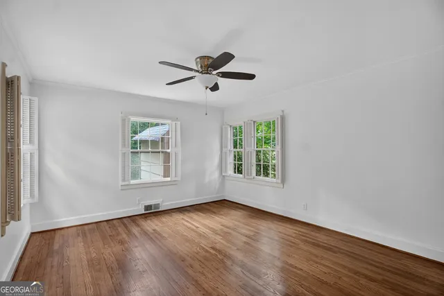 an empty room with wooden floor ceiling fan and windows