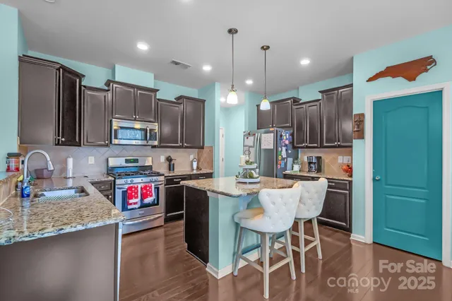 a kitchen with stainless steel appliances kitchen island granite countertop a sink a stove a refrigerator and chairs