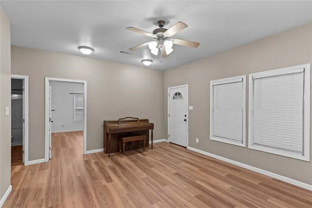 an empty room with wooden floor fan and windows
