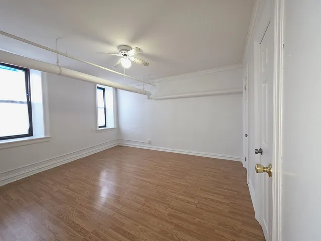 an empty room with wooden floor fan and windows