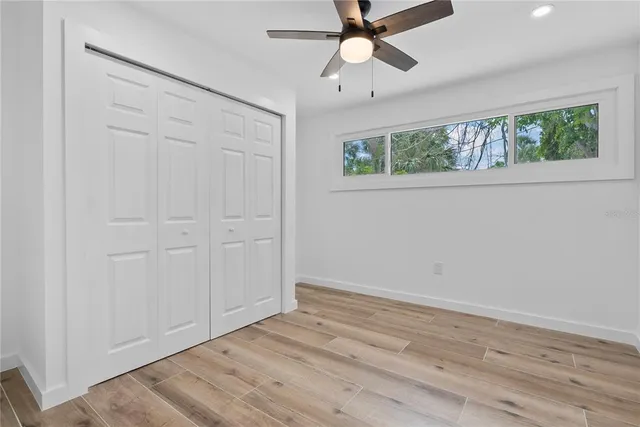 an empty room with wooden floor fan and windows