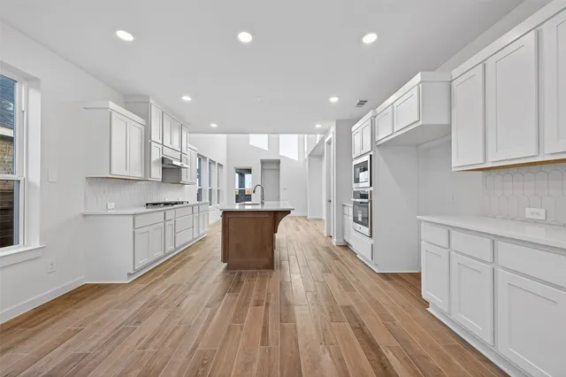 a large kitchen with stainless steel appliances granite countertop a large center island a sink dishwasher a refrigerator and white cabinets with wooden floor