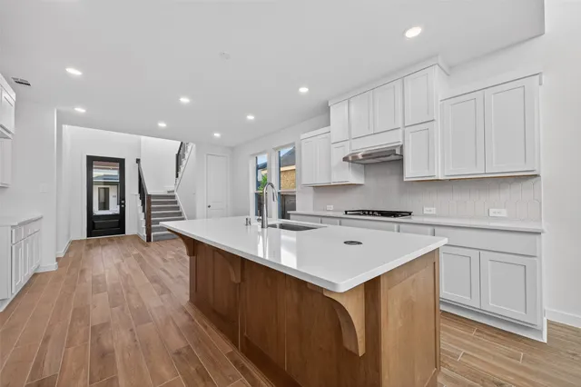 a kitchen with stainless steel appliances granite countertop a sink stove and white cabinets with wooden floor