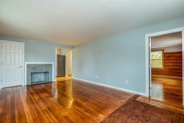 an empty room with wooden floor fireplace and windows