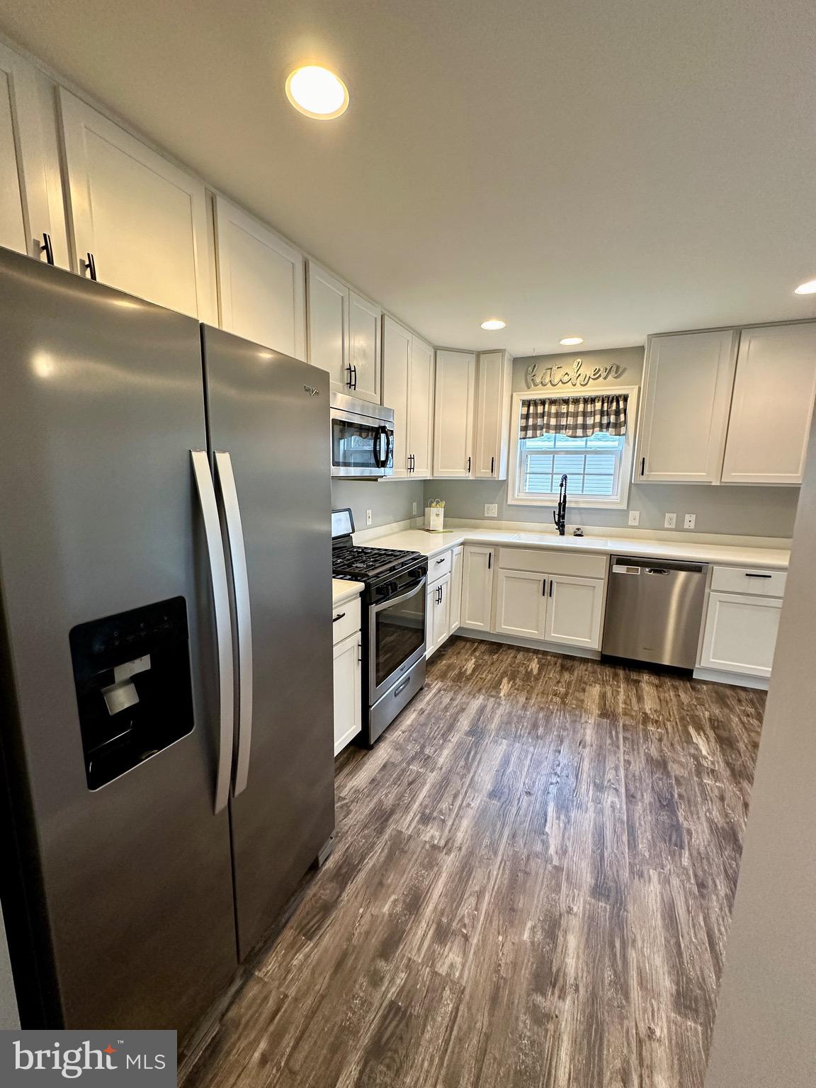 326 Sweeping Mist Circle Frederica, DE 19946 - Photo 17 of 37 a kitchen with stainless steel appliances granite countertop a refrigerator a sink dishwasher a stove and white countertops with wooden floor