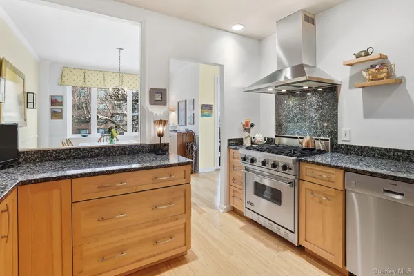 a kitchen with stainless steel appliances granite countertop a refrigerator a stove a sink and white cabinets with wooden floor