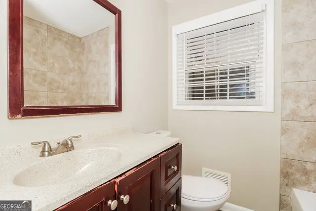 a bathroom with a granite countertop sink toilet a mirror and a window