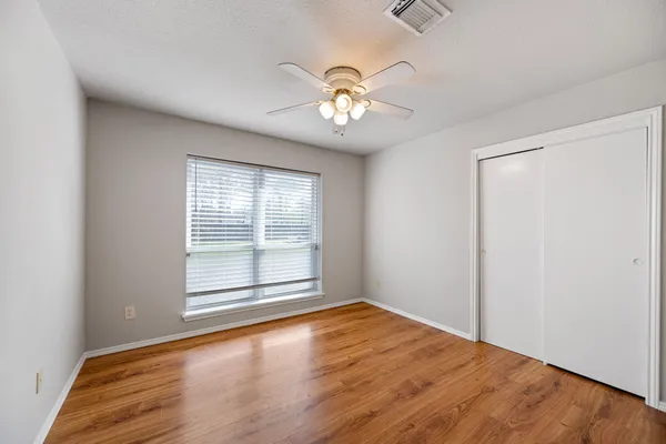 an empty room with wooden floor chandelier fan and windows