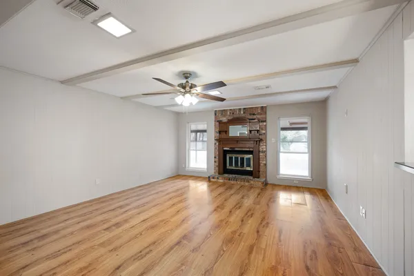 a view of an empty room with wooden floor fireplace and a window