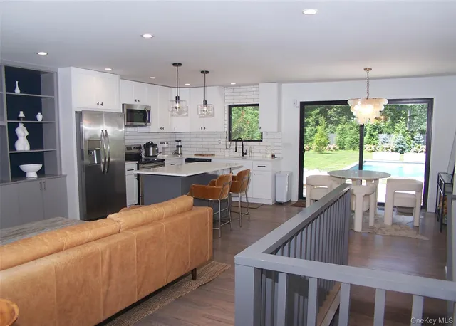 a kitchen with stainless steel appliances kitchen island granite countertop a refrigerator a sink a stove and a dining table with wooden floor