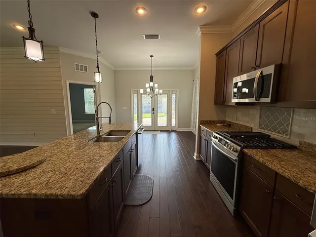 a kitchen with kitchen island granite countertop a stove a sink a refrigerator wooden floor and cabinets