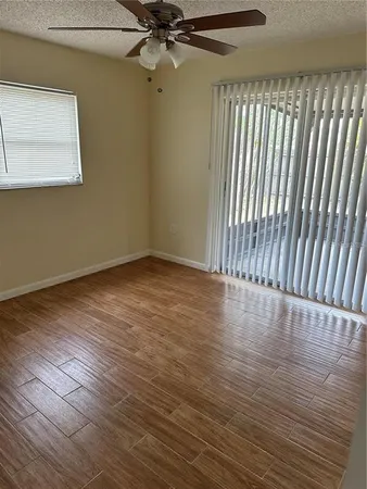 an empty room with wooden floor fan and windows