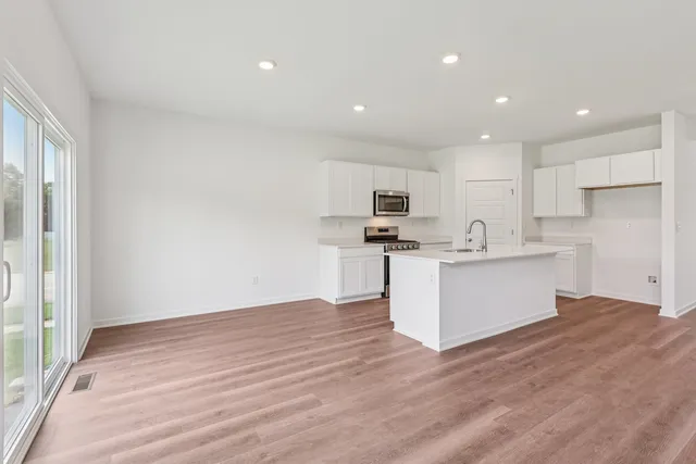 a large white kitchen with kitchen island a sink wooden floor and stainless steel appliances
