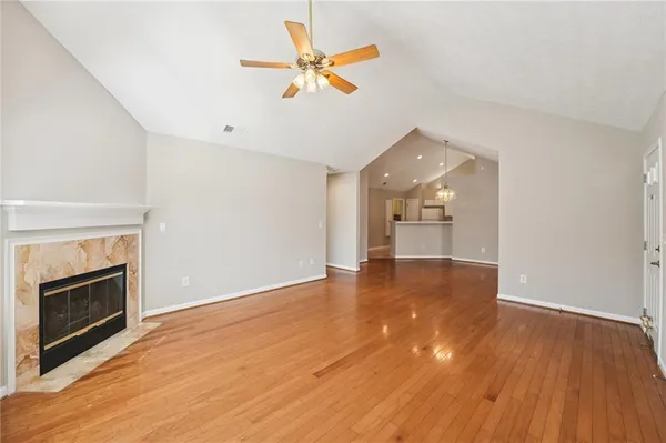 an empty room with wooden floor a ceiling fan a fireplace and windows